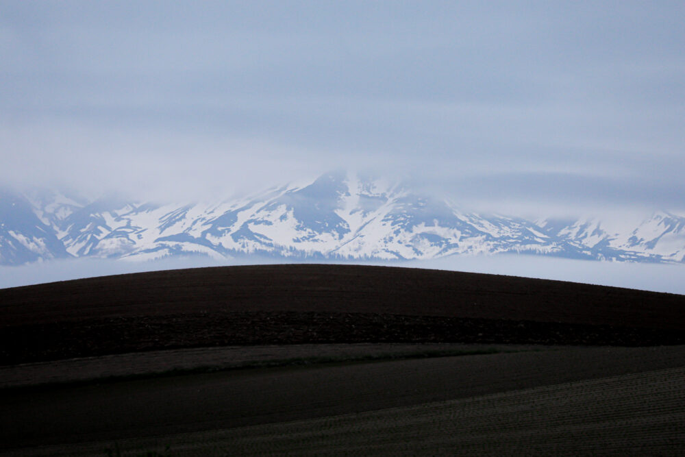 雪が残る十勝岳連邦と丘陵の畑